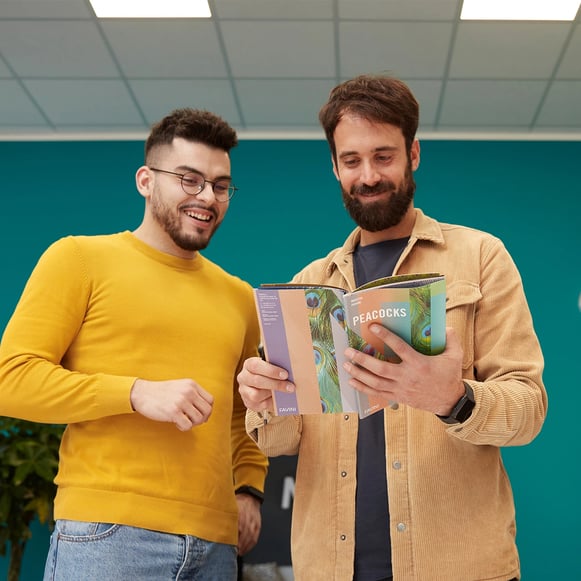 Art director e designer che sfogliano sorridendo un manuale di riferimento.