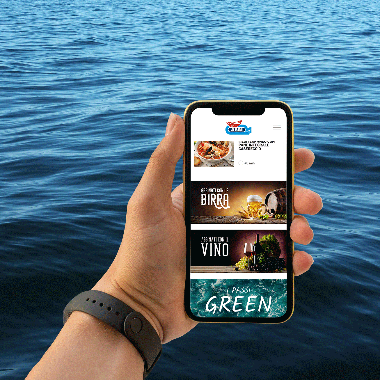 Davanti al mare, una mano regge uno smartphone che alterna immagini del sito di Arbi.