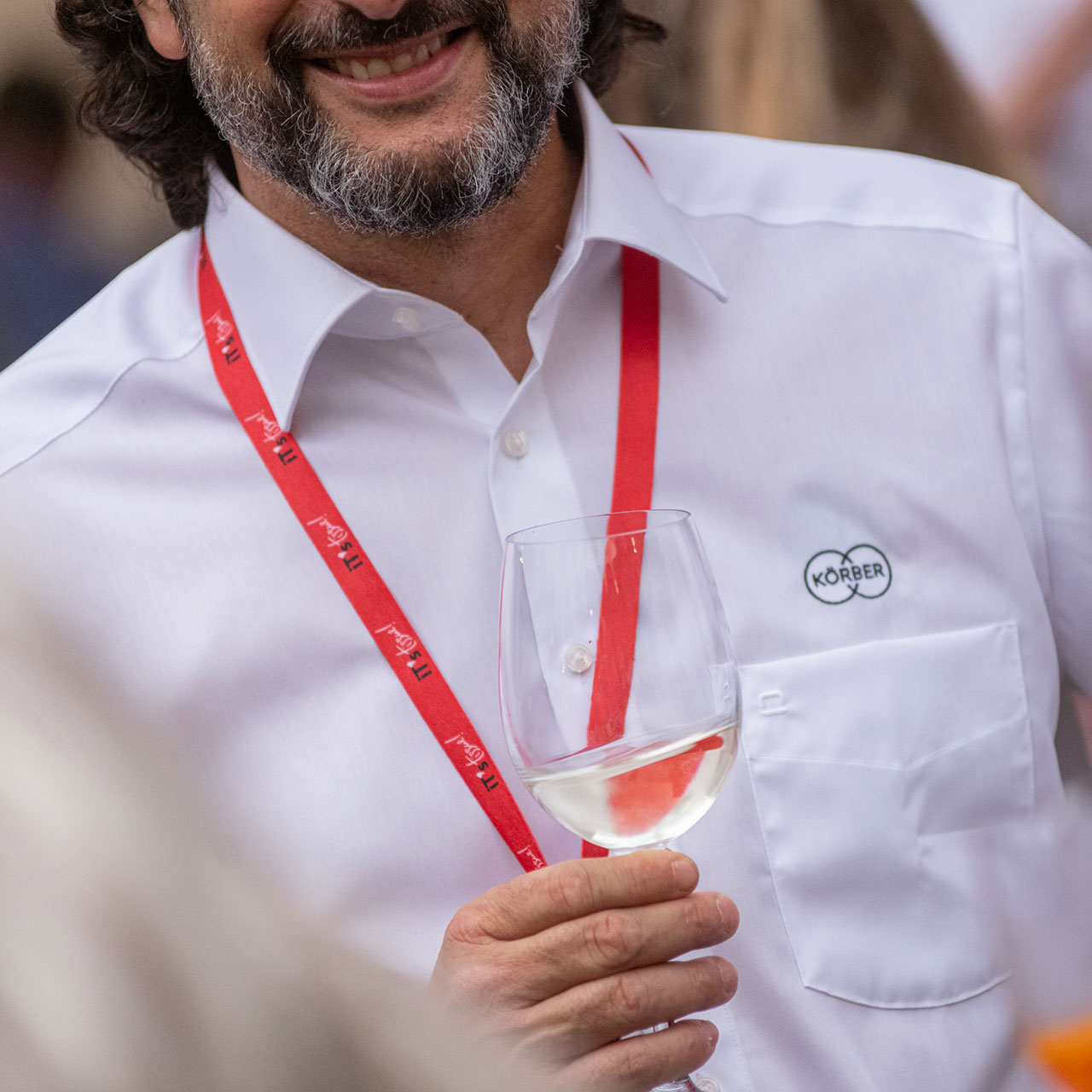 Uomo in camicia bianca mentre regge un calice di vino bianco. 